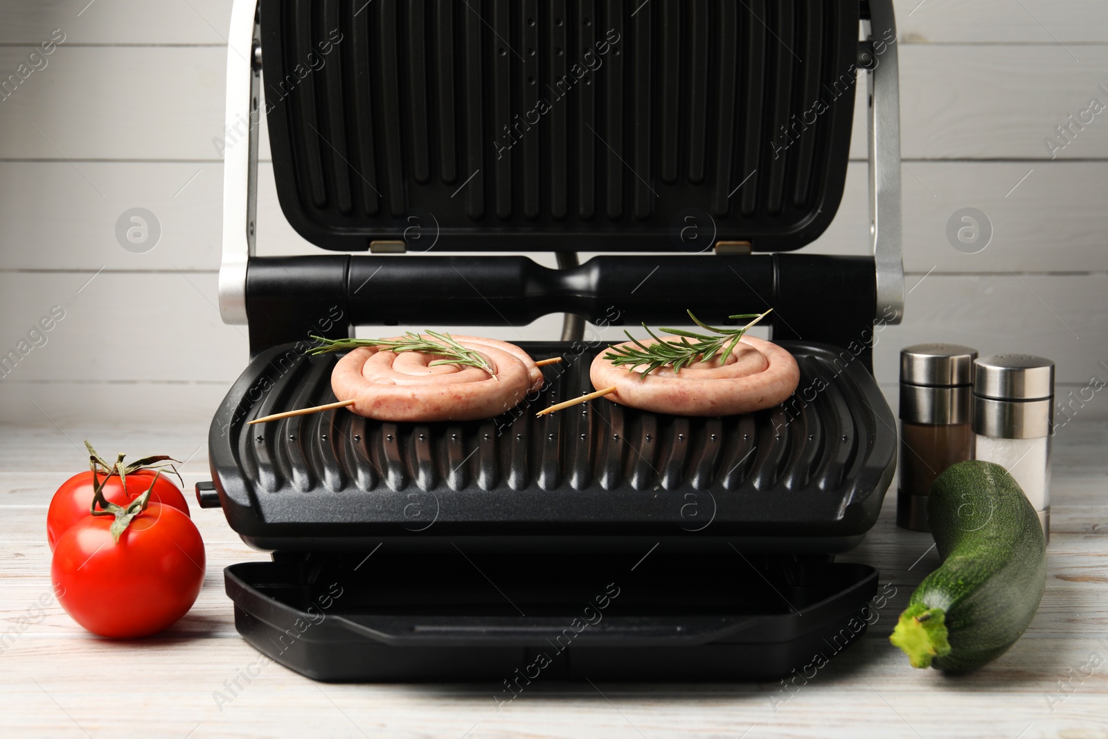 Photo of Electric grill with homemade sausages, rosemary, vegetables and spices on wooden table