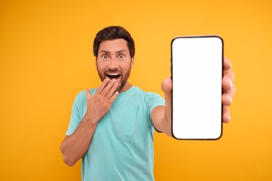 Surprised man showing smartphone in hand on yellow background