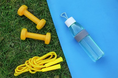 Photo of Skipping rope, dumbbells, fitness mat and bottle of water on green grass, flat lay. Morning exercise