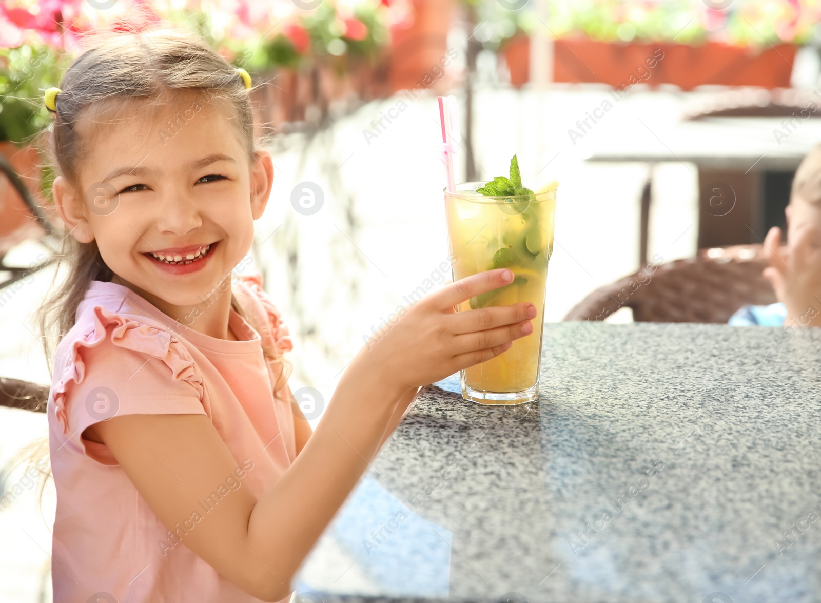 Photo of Cute girl with glass of natural lemonade at table in cafe