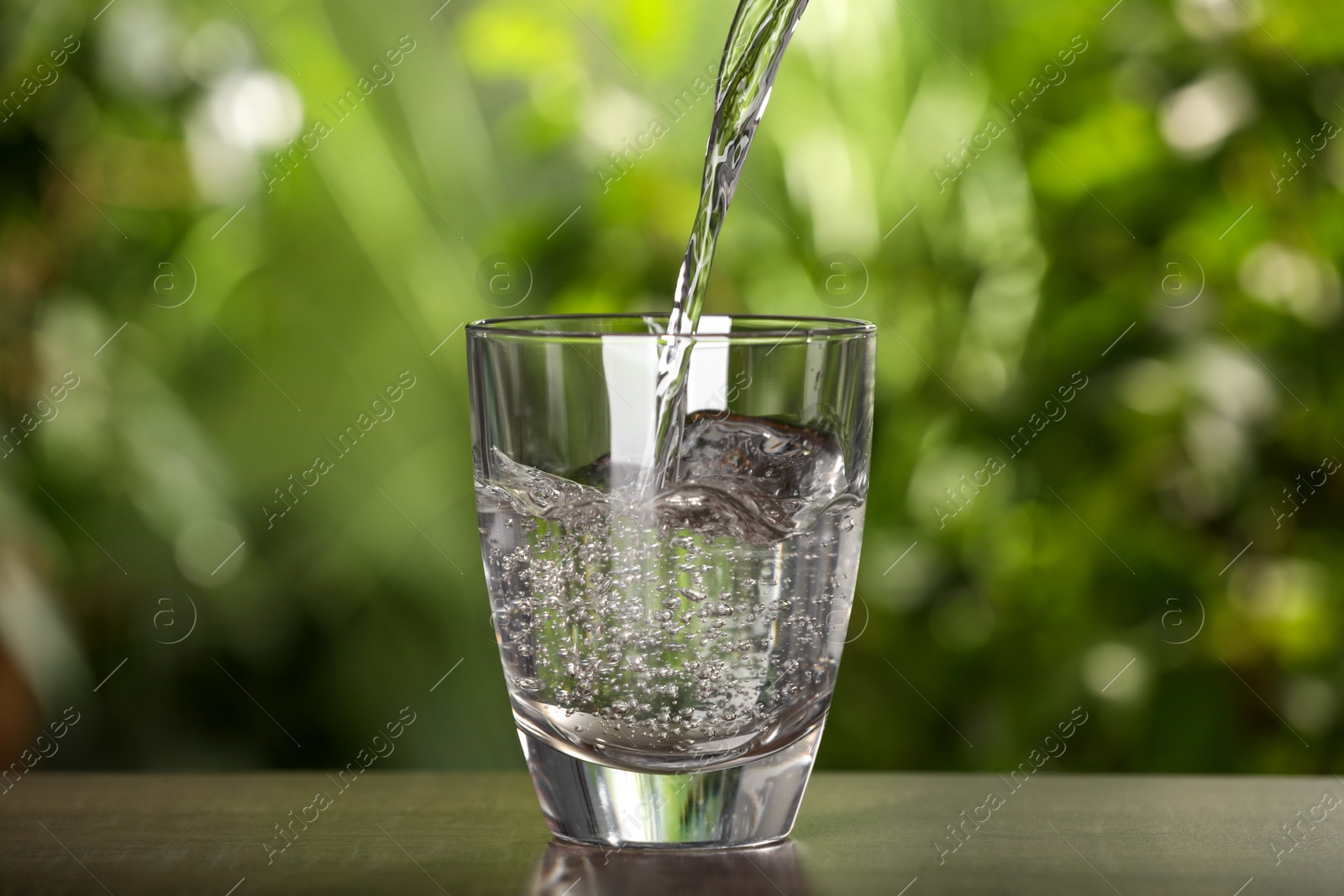 Photo of Pouring water into glass on light grey table outdoors