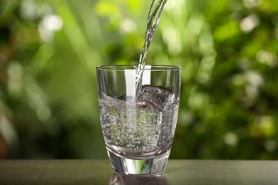 Pouring water into glass on light grey table outdoors