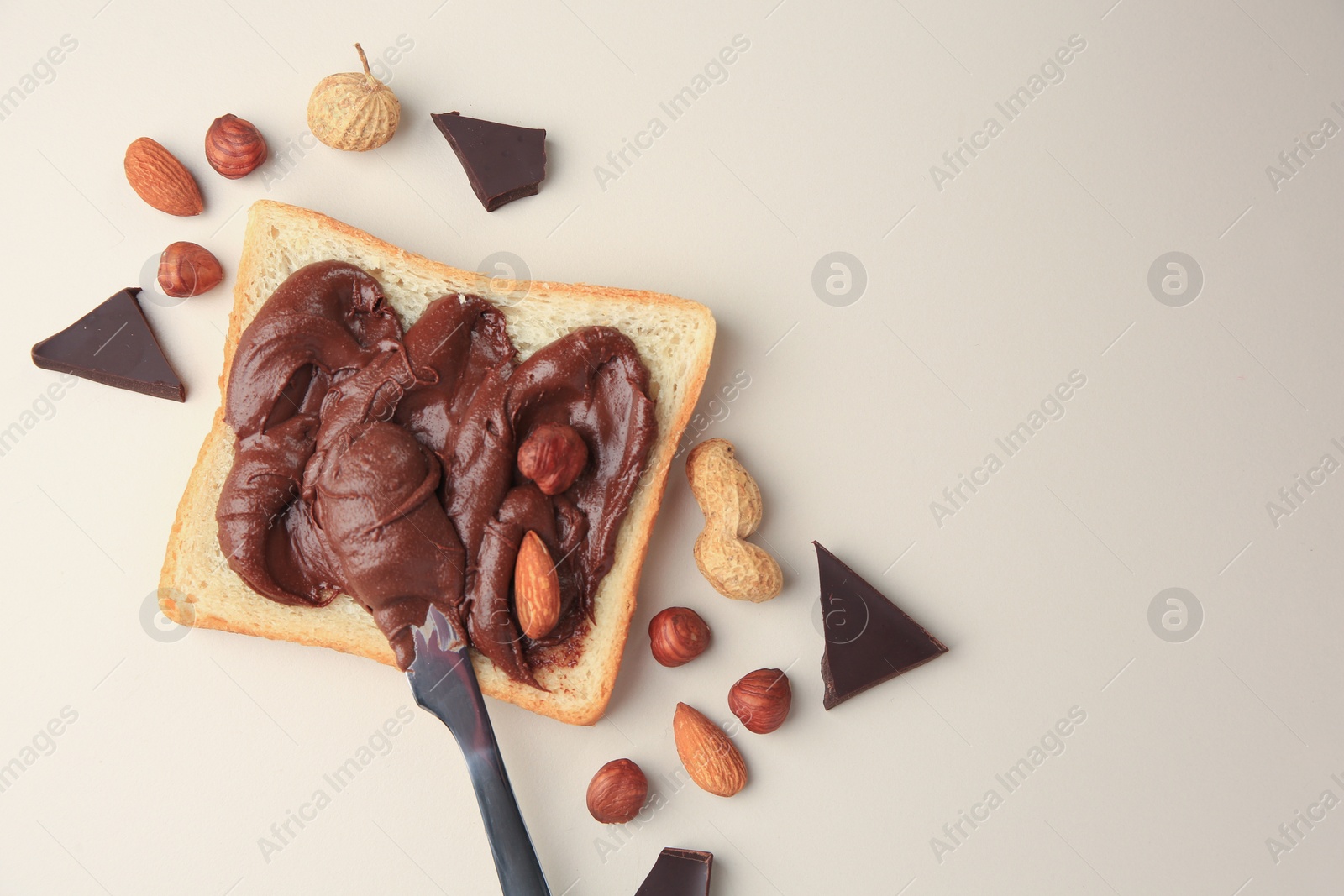 Photo of Tasty toast with chocolate paste and nuts on beige background, flat lay. Space for text