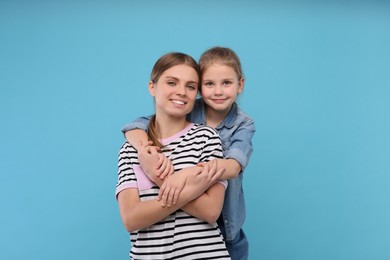 Little daughter hugging her mom on light blue background. Happy Mother's Day