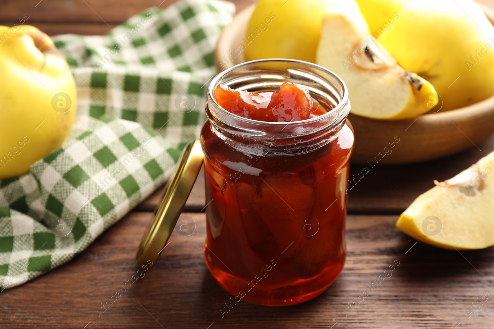 Photo of Tasty homemade quince jam in jar and fruits on wooden table, closeup