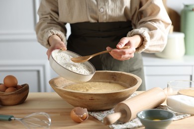 Making dough. Woman adding flour into bowl at wooden table in kitchen, closeup