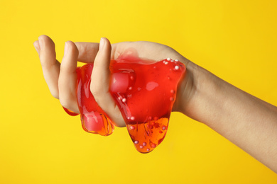 Photo of Woman playing with red slime on yellow background, closeup. Antistress toy