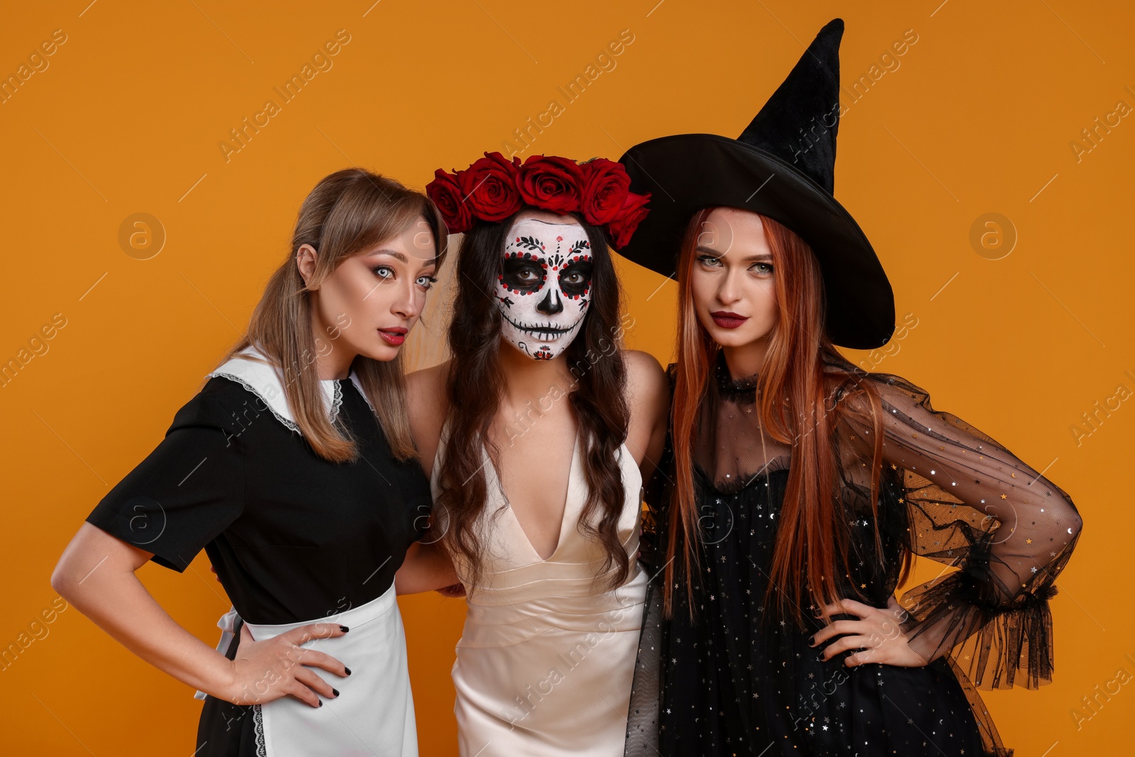 Photo of Women in scary costumes on orange background. Halloween celebration