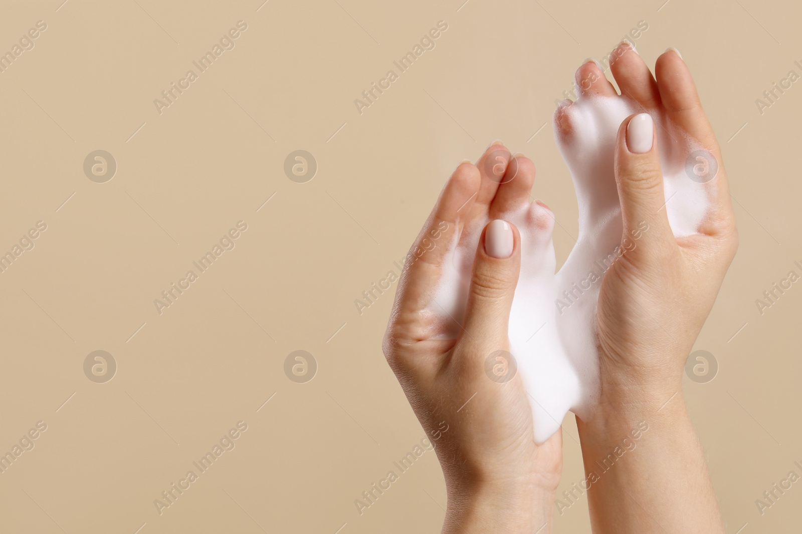 Photo of Skin care cosmetic. Woman washing hands with cleansing foam on beige background, closeup and space for text