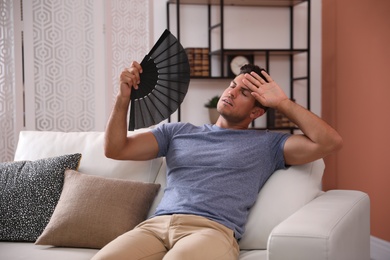 Photo of Man with hand fan sitting on sofa. Summer season