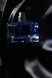 Photo of Luxury men's perfume in bottle on black satin fabric, top view. Space for text