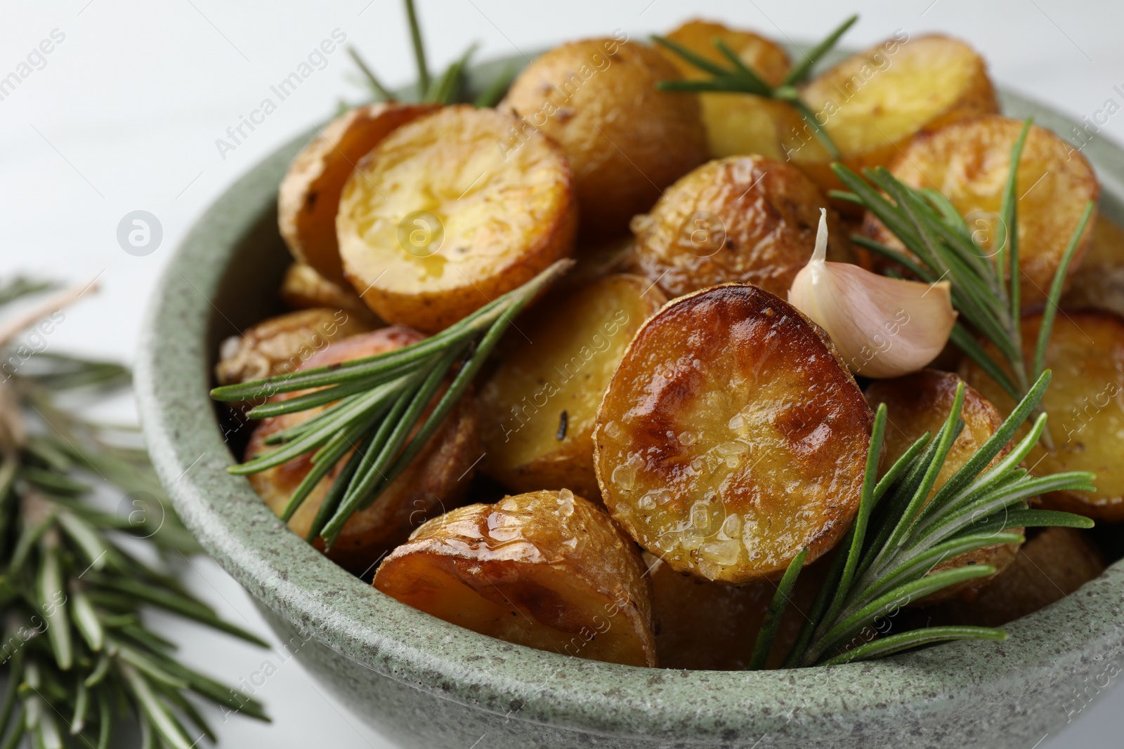 Photo of Bowl with tasty baked potato and aromatic rosemary on white table, closeup