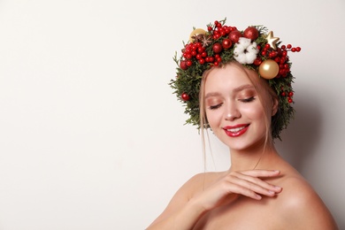 Beautiful young woman wearing Christmas wreath on white background. Space for text