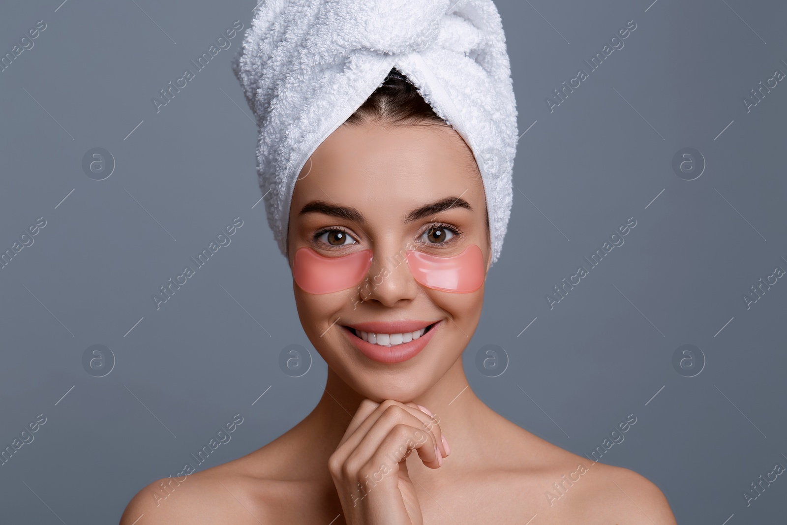 Photo of Beautiful young woman with under eye patches and hair wrapped in towel on grey background