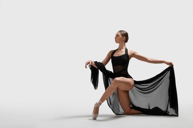 Photo of Graceful young ballerina practicing dance moves with black veil on white background. Space for text