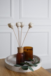 Photo of Reed air freshener with candle and eucalyptus branch on tray indoors