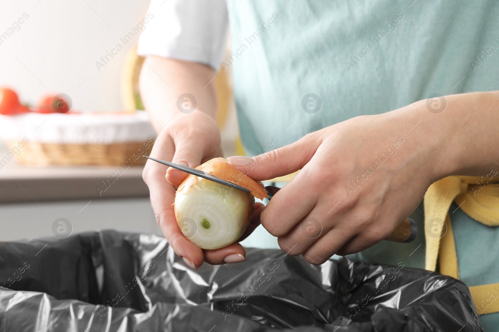 Photo of Woman peeling fresh onion with knife above garbage bin indoors, closeup