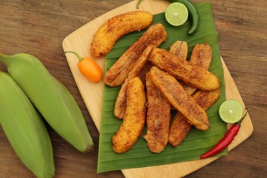 Photo of Delicious fried bananas, different peppers and cut limes on wooden table, flat lay