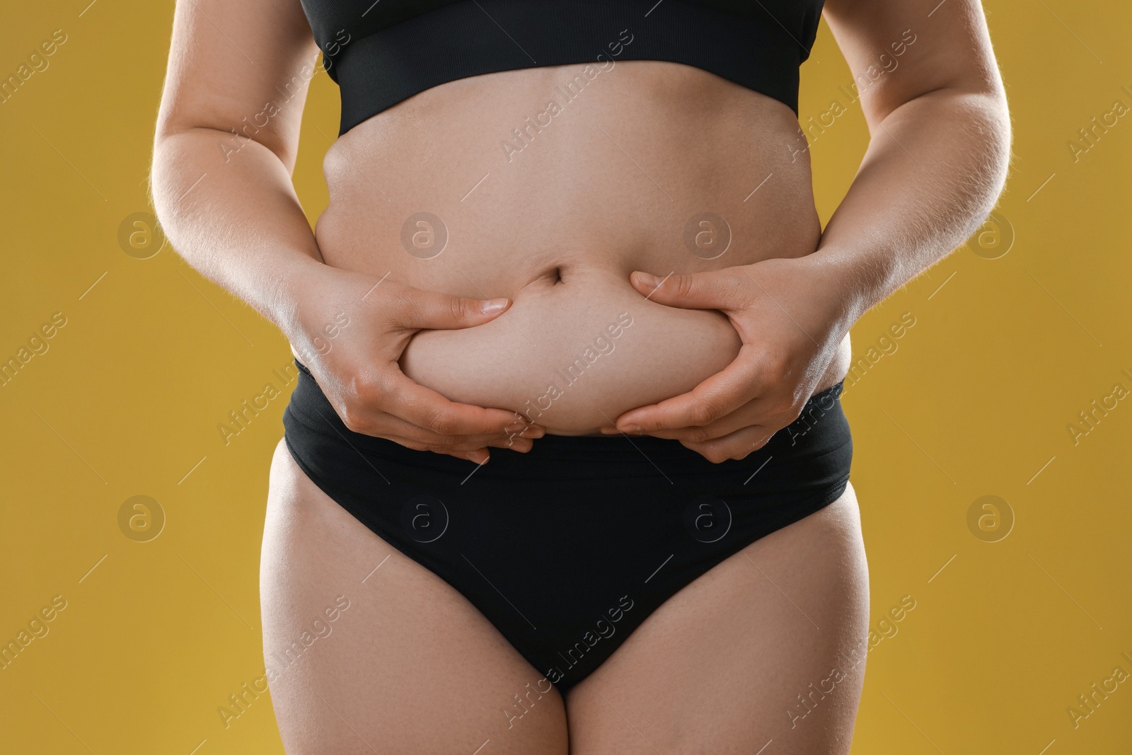 Photo of Woman touching belly fat on goldenrod background, closeup. Overweight problem