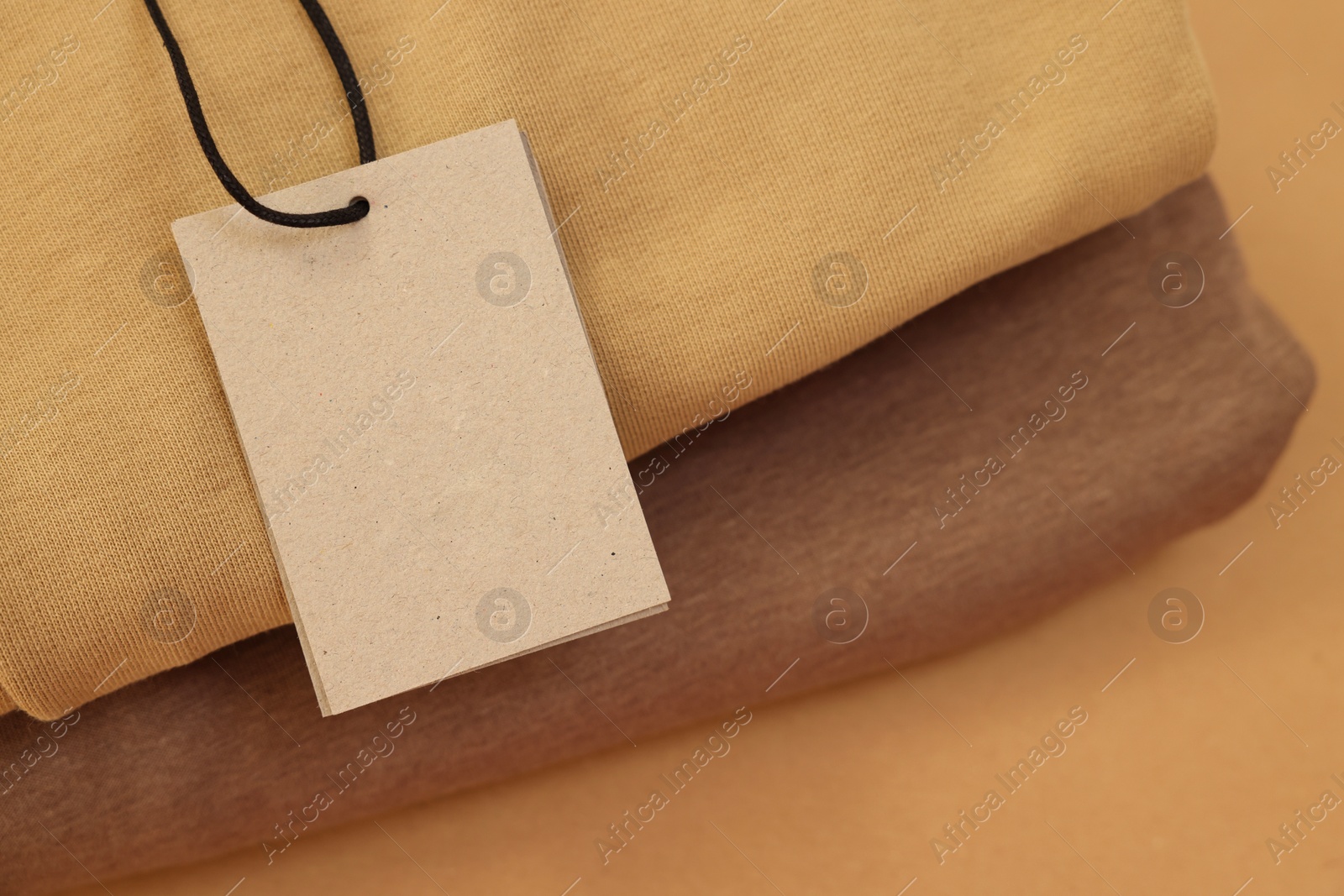 Photo of Garment with cardboard tag on beige background, closeup. Space for text