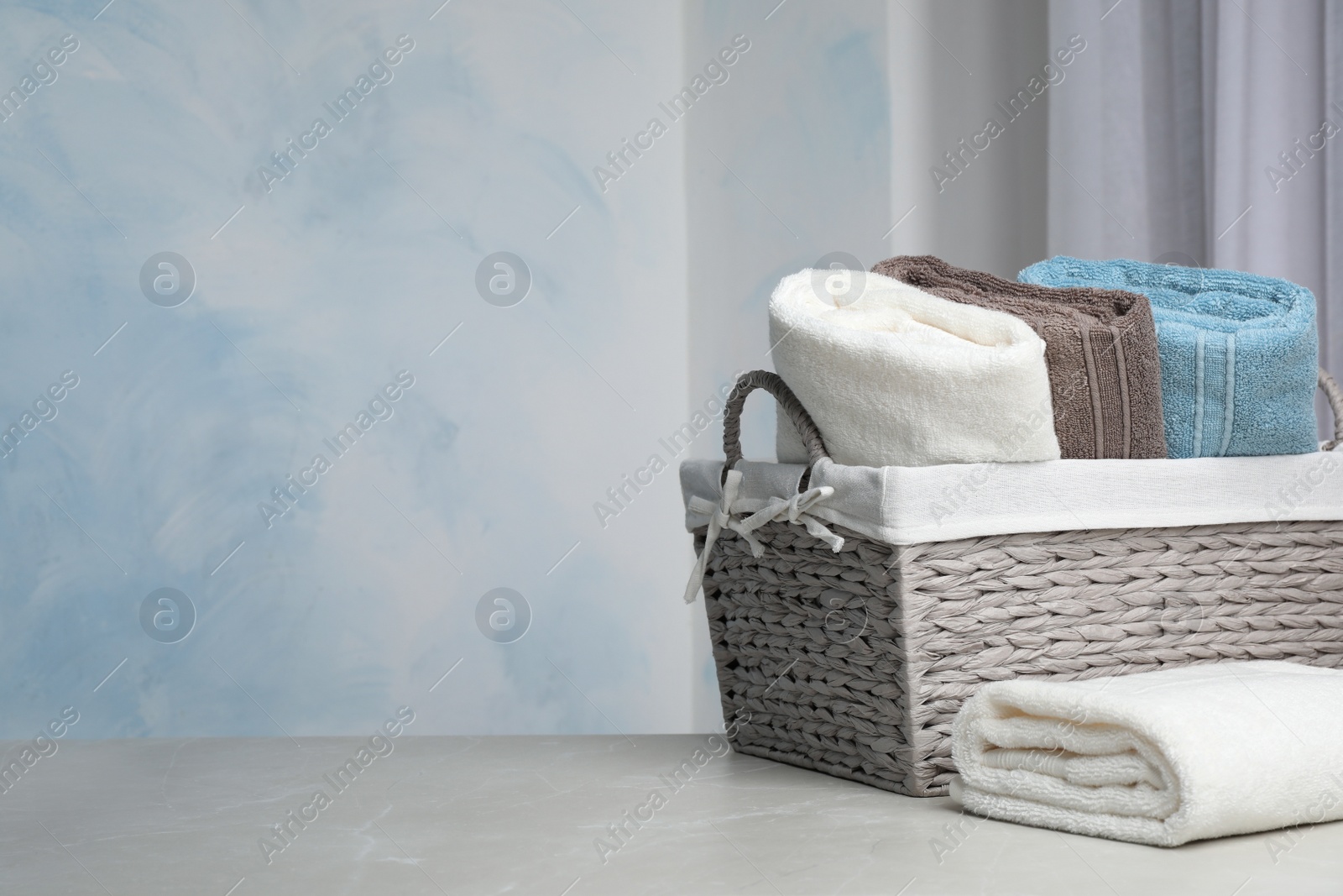 Photo of Basket and soft bath towels on table against blurred background. Space for text