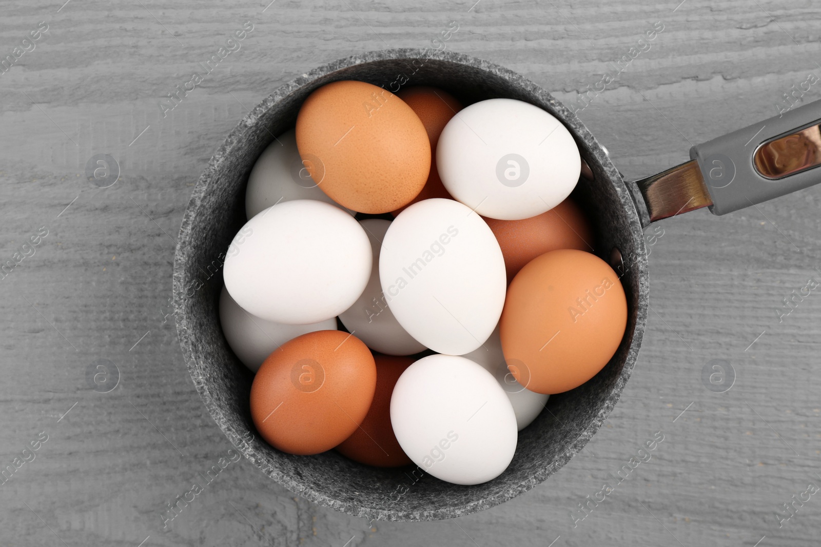 Photo of Unpeeled boiled eggs in saucepan on grey wooden table, top view