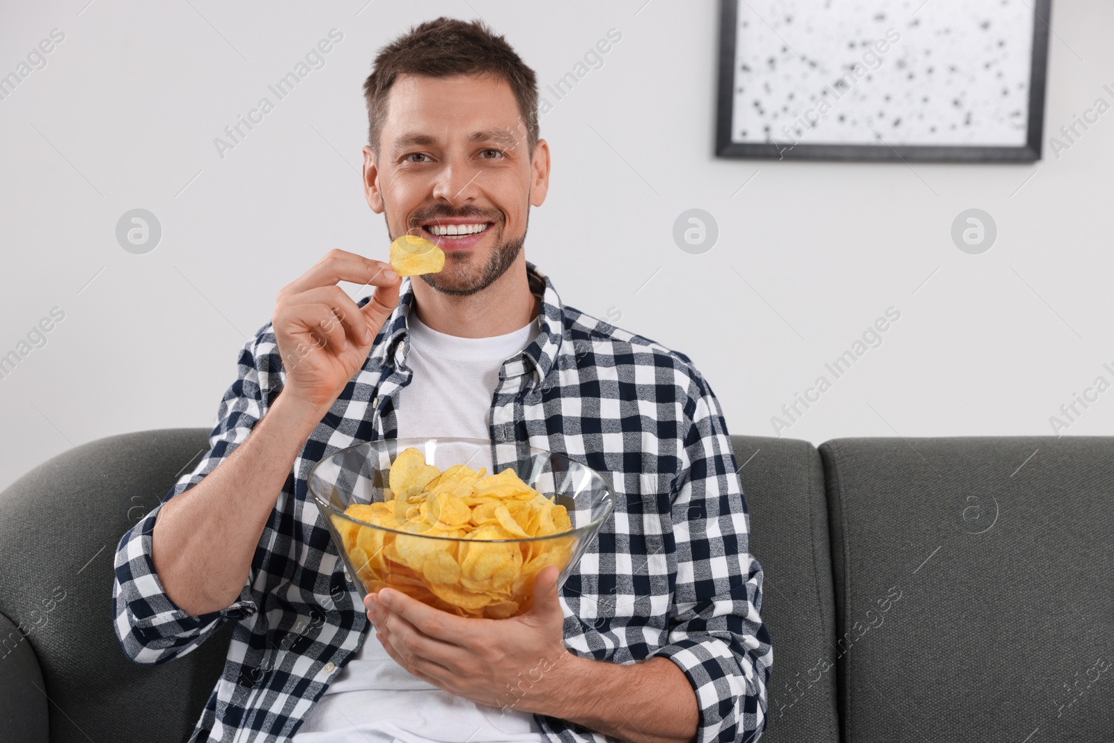 Photo of Handsome man eating potato chips on sofa at home