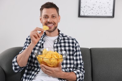 Handsome man eating potato chips on sofa at home