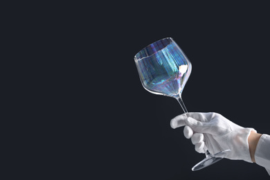 Photo of Person in white glove checking cleanliness of glass on dark background, closeup. Space for text