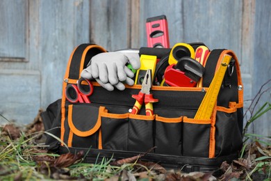 Photo of Bag with different tools for repair on grass near wooden door outdoors