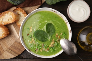 Photo of Delicious broccoli cream soup with basil and pumpkin seeds served on wooden table, flat lay