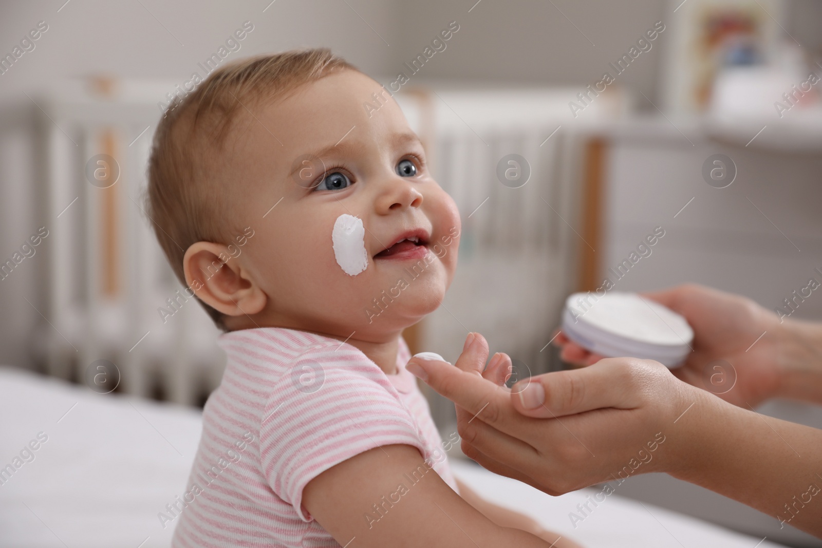 Photo of Mother applying moisturizing cream on her little baby at home, closeup