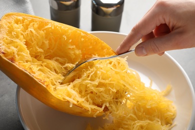 Photo of Woman scraping flesh of cooked spaghetti squash with fork at table, closeup
