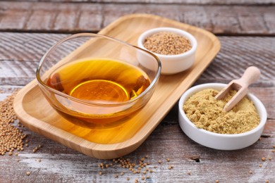 Photo of Bowl of natural oil, mustard seeds and powder on wooden table, closeup