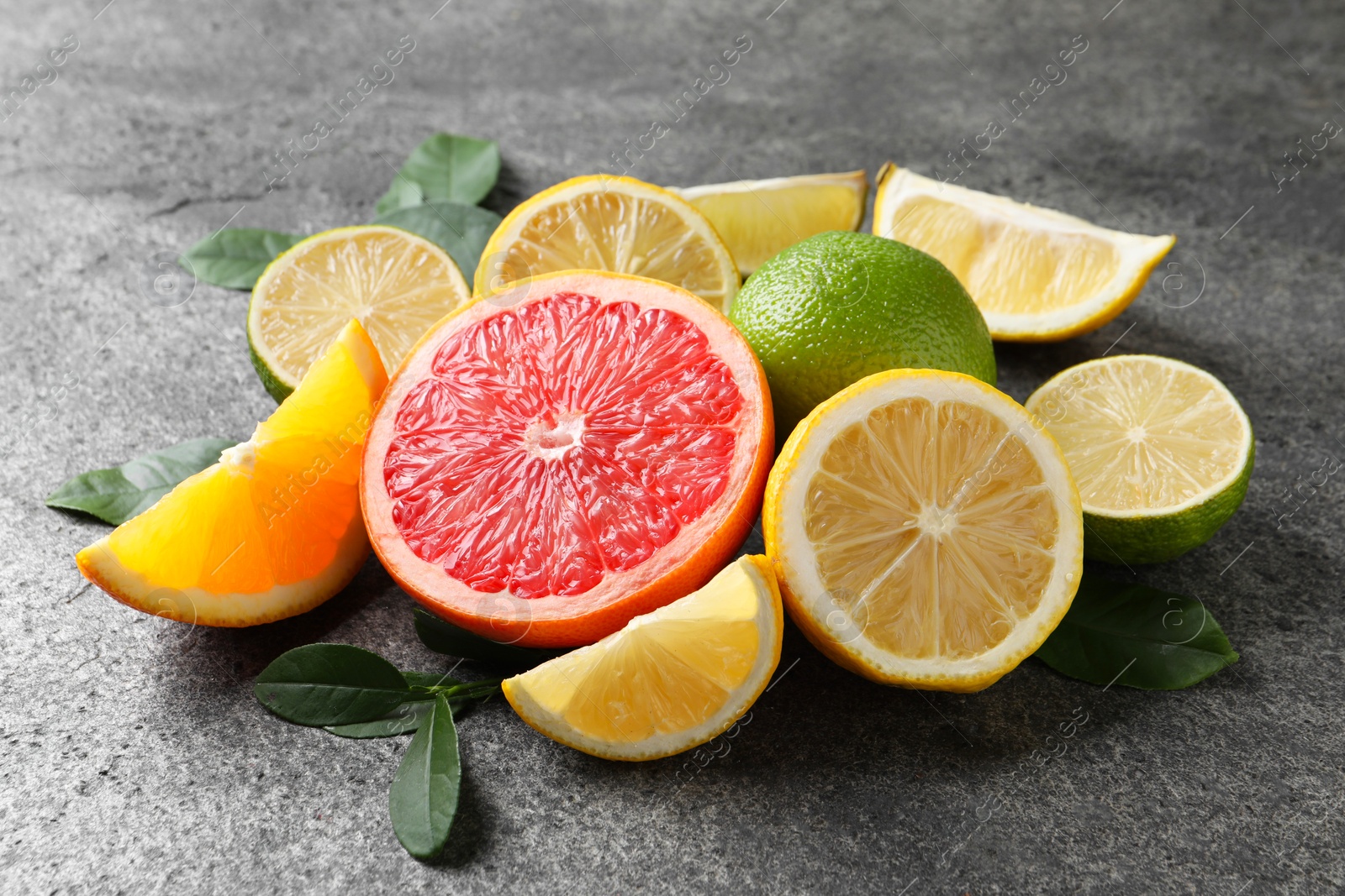 Photo of Different fresh citrus fruits and leaves on grey textured table, closeup