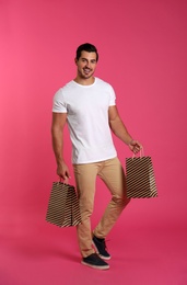 Young handsome man holding paper bags on pink background. Mockup for design