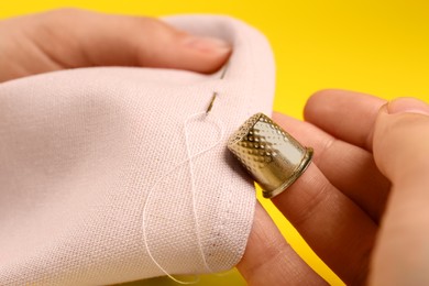 Photo of Woman sewing on pink fabric with thimble and needle against yellow background, closeup