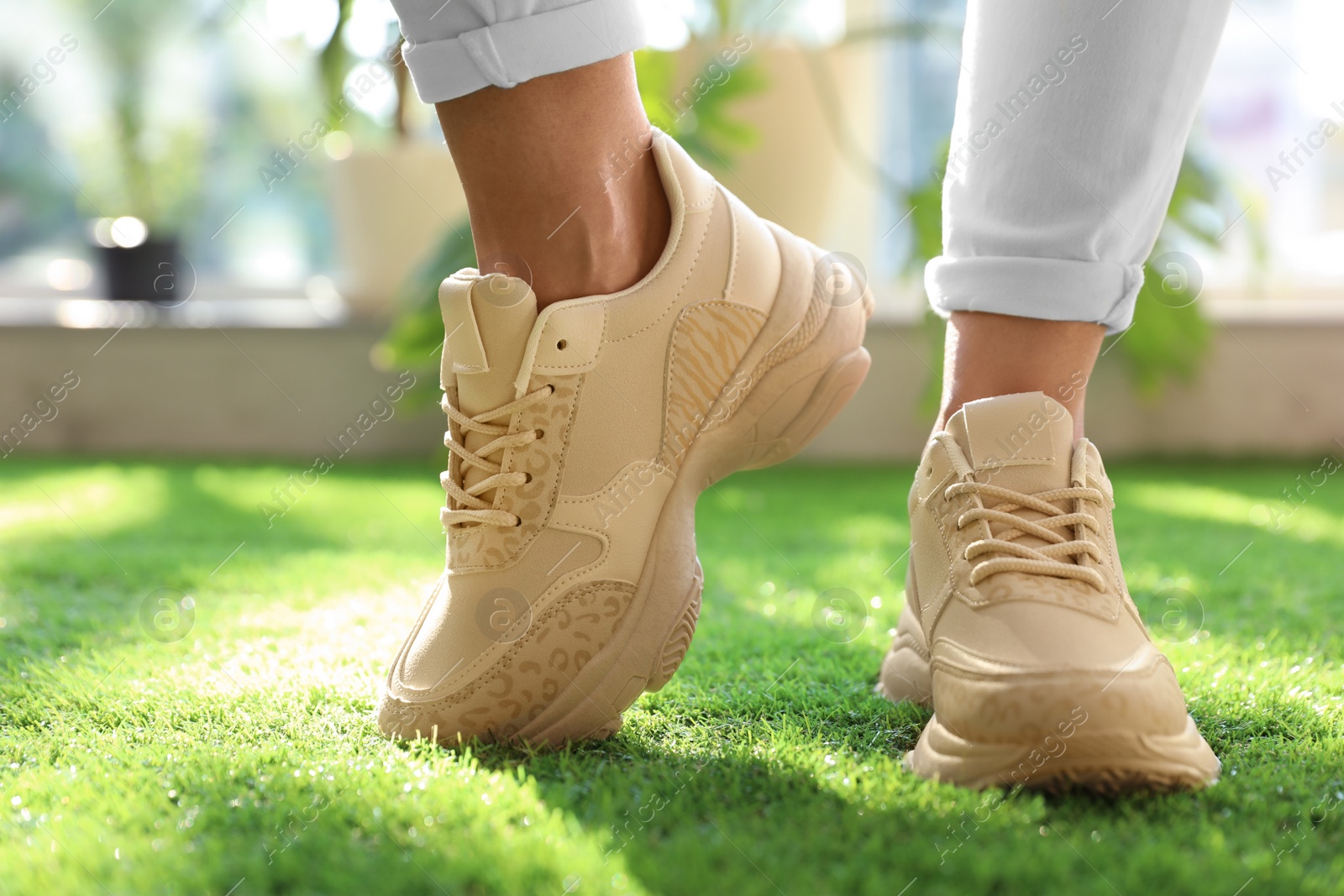 Photo of Young woman wearing stylish sneakers on green grass, closeup