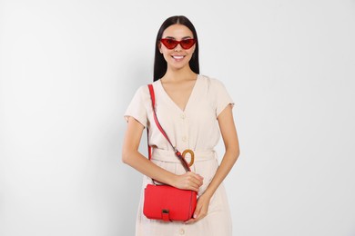 Photo of Beautiful young woman with red bag in stylish sunglasses on light grey background