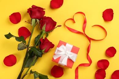 Photo of Flat lay composition with beautiful red roses and gift box on yellow background. Valentine's Day celebration