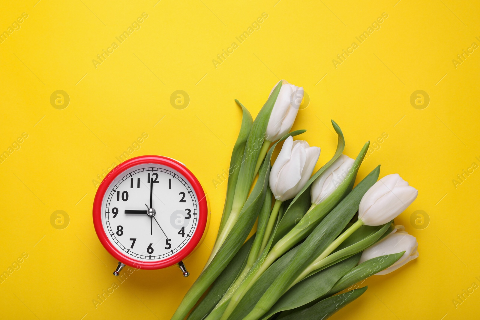Photo of Red alarm clock and beautiful tulips on yellow background, flat lay. Spring time