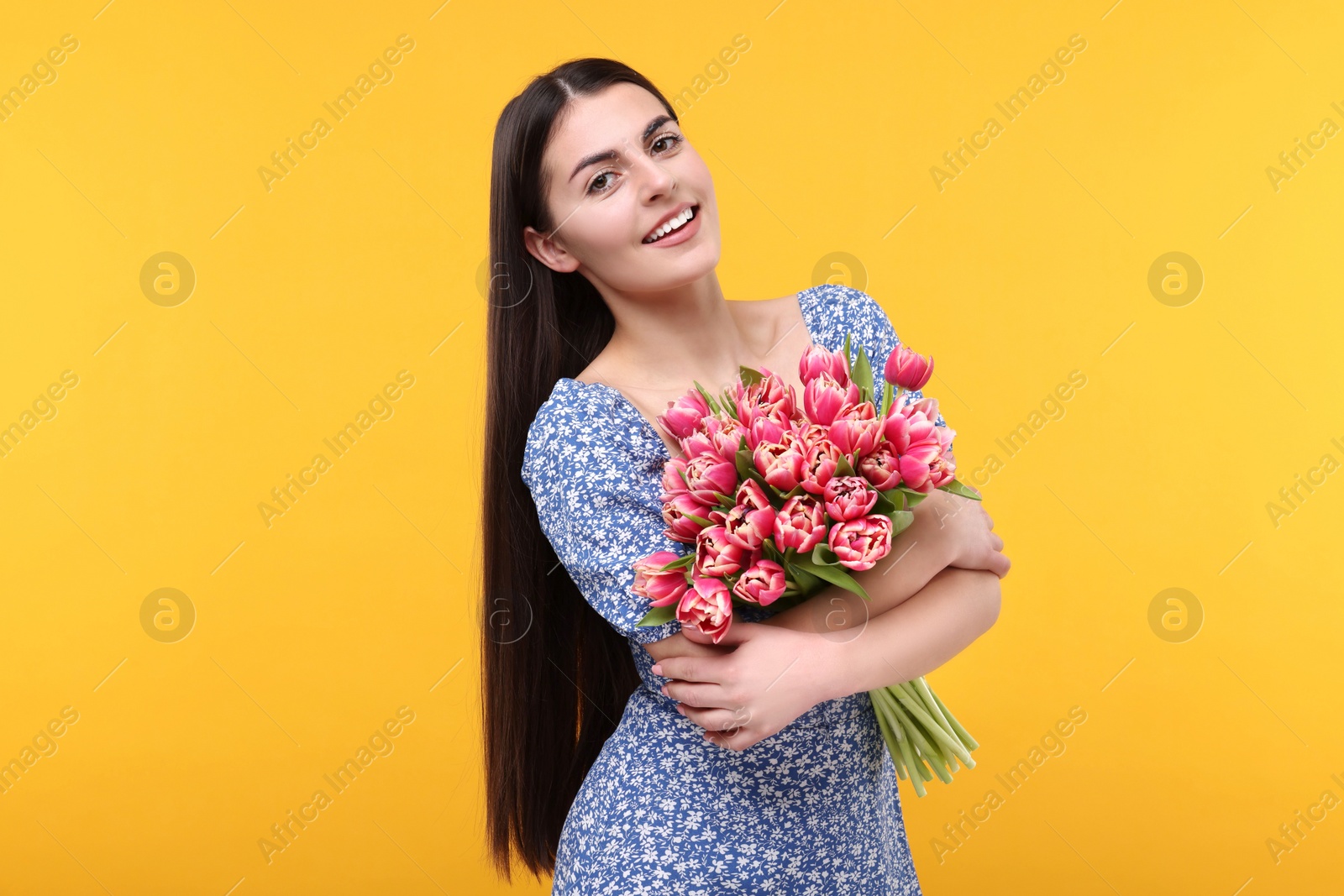 Photo of Happy young woman with beautiful bouquet on orange background