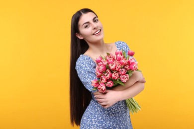 Photo of Happy young woman with beautiful bouquet on orange background