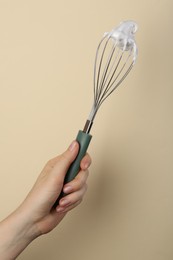 Woman holding whisk with whipped cream on beige background, closeup