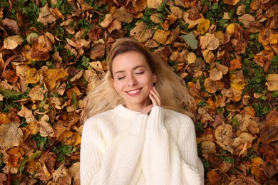 Photo of Smiling woman lying among autumn leaves outdoors, top view