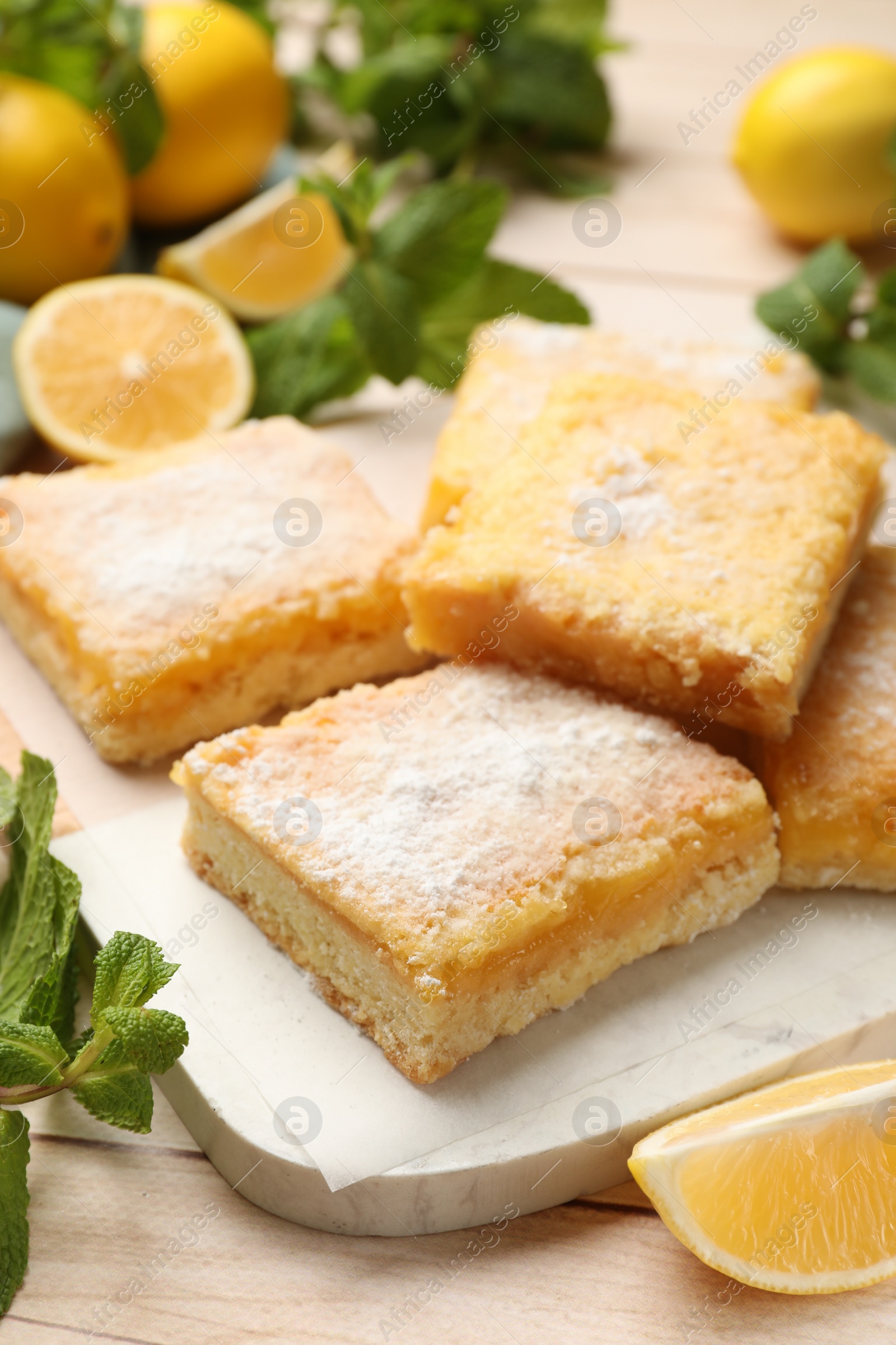 Photo of Tasty lemon bars with powdered sugar and mint on wooden table, closeup