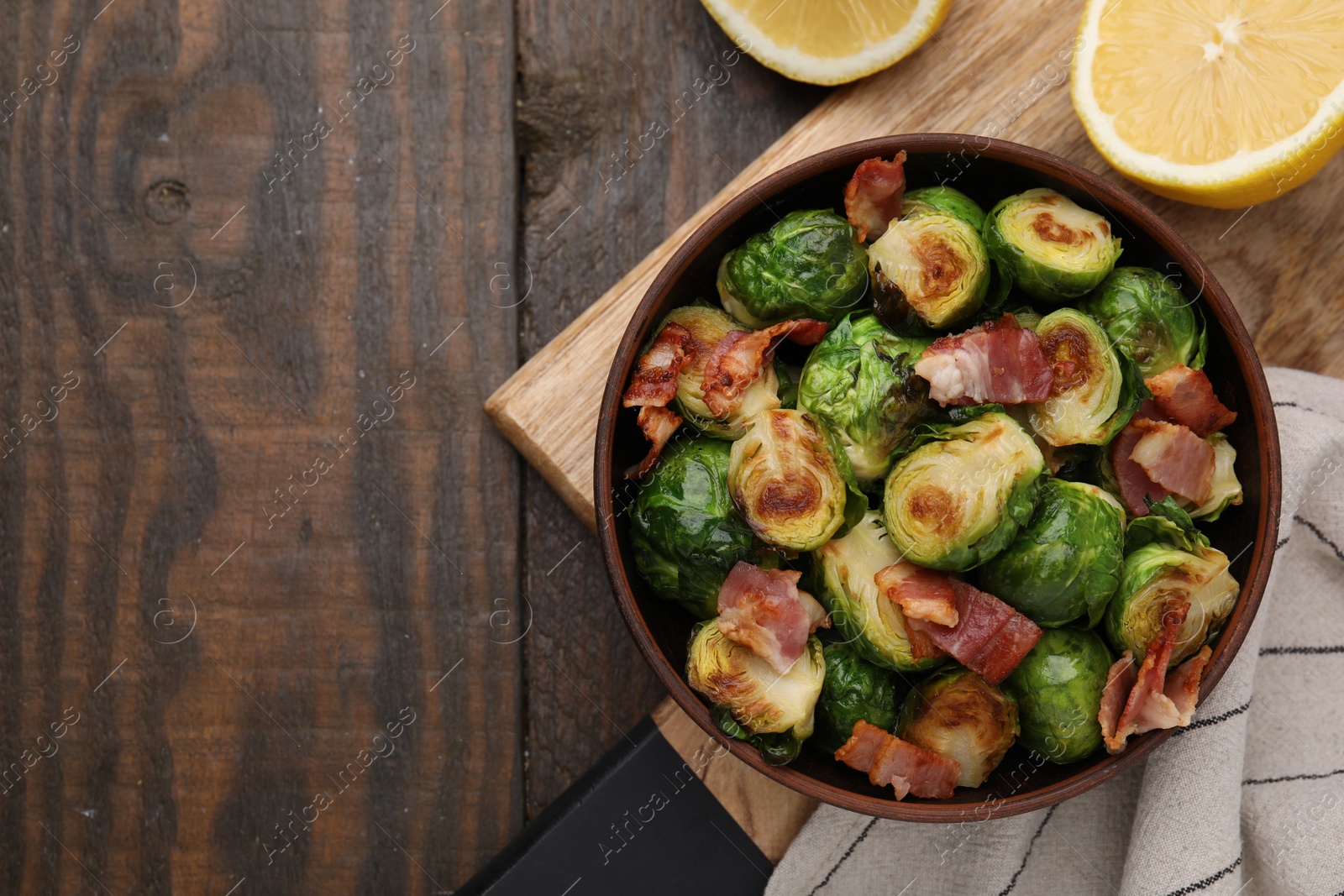 Photo of Delicious roasted Brussels sprouts, bacon and lemon on wooden table, top view. Space for text