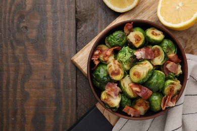 Photo of Delicious roasted Brussels sprouts, bacon and lemon on wooden table, top view. Space for text