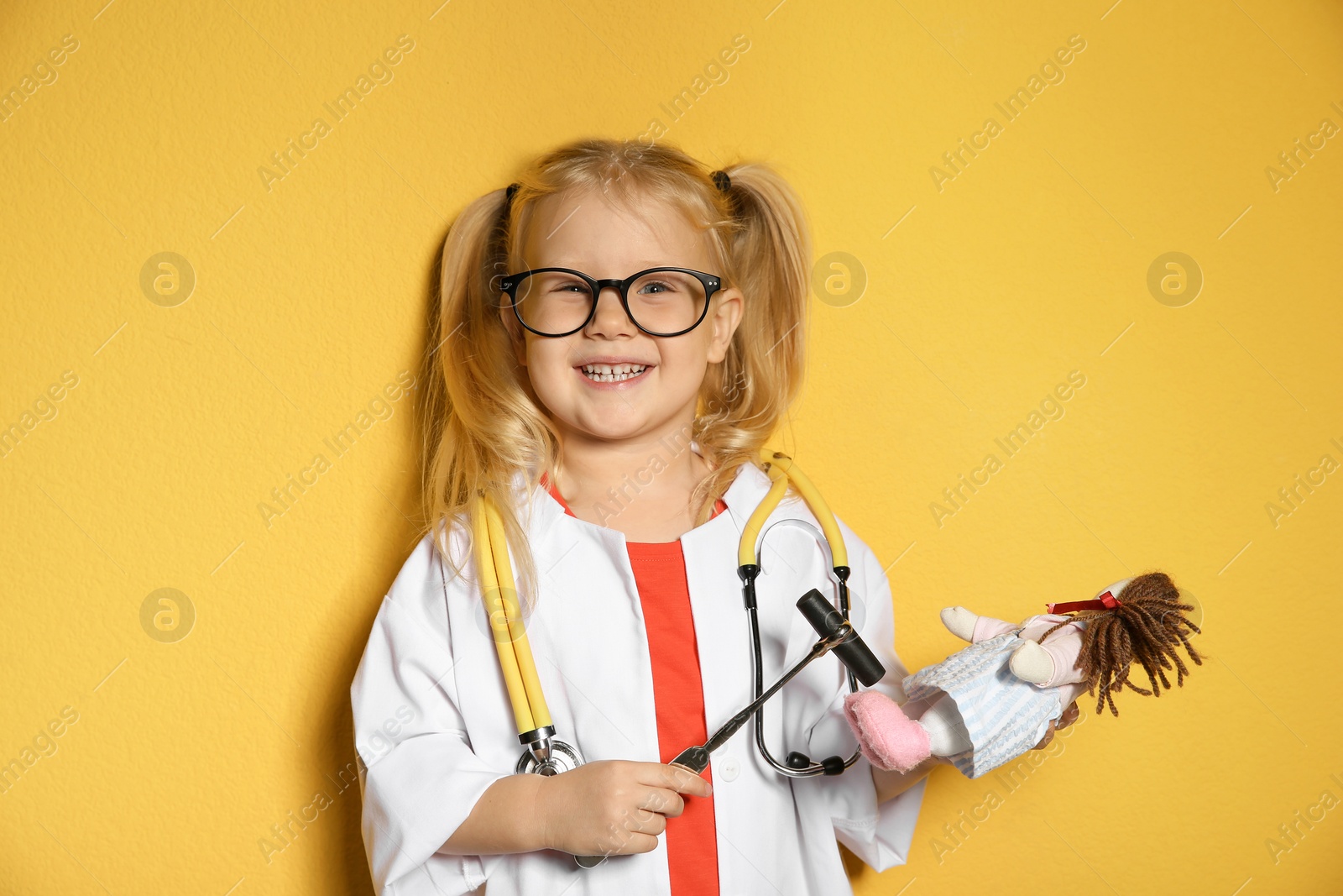 Photo of Cute child imagining herself as doctor while playing with reflex hammer and doll on color background