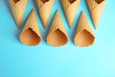 Photo of Empty wafer ice cream cones on blue background, flat lay. Space for text